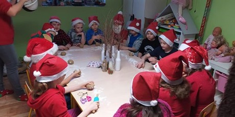 Powiększ grafikę: Uczniowie klasy 1 ubrani w mikołajkowe stroje siedzą przy stole i robią pierniczki. 