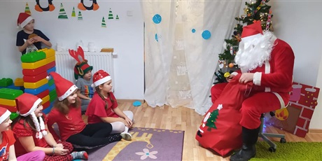 Powiększ grafikę: Uczniowie ubrani w mikołajkowe stroje w towarzystwie Mikołaja który daje im prezenty.
